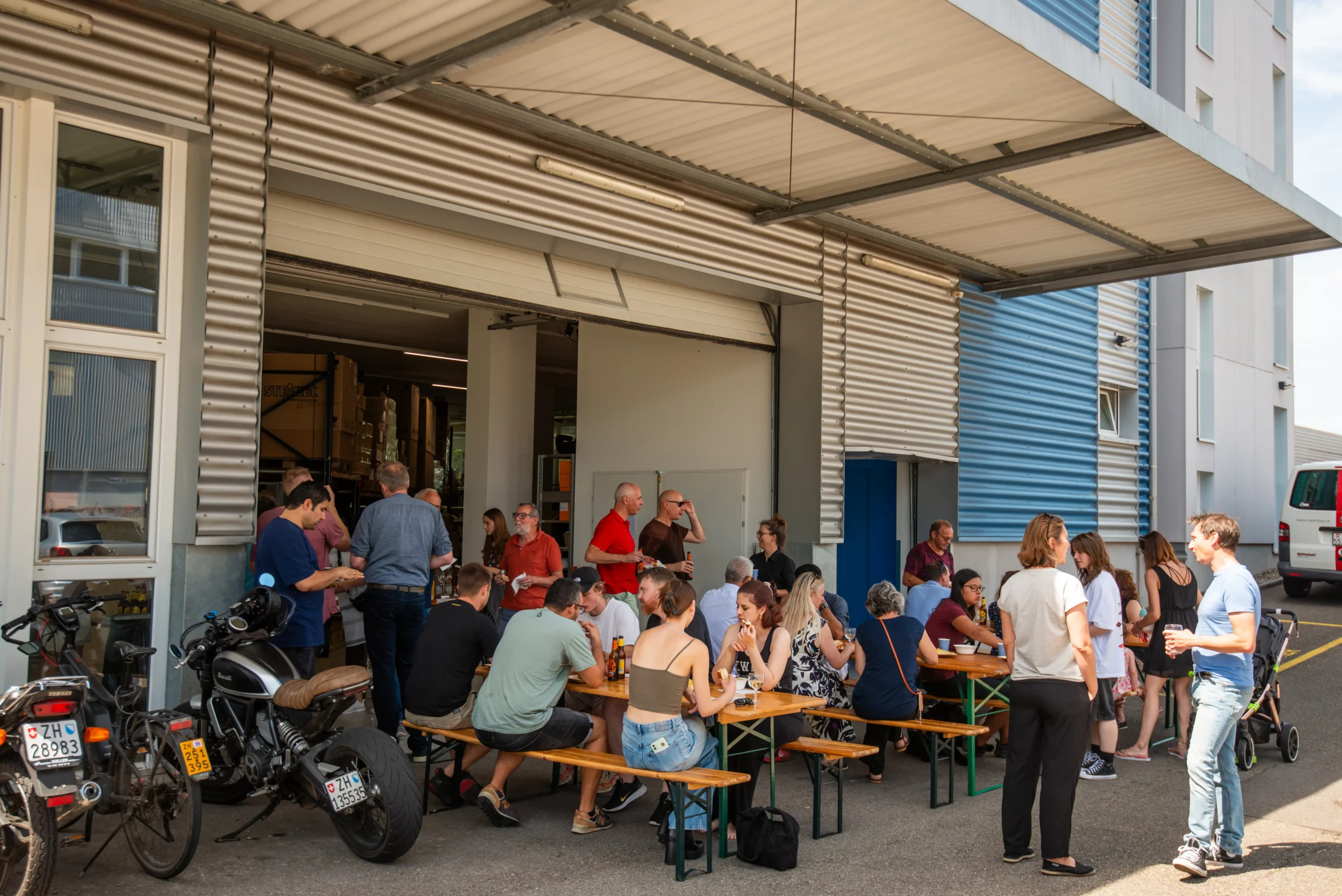 Der Apero nach der Gautschete 2024 von Janis Rüdisüli und Laura Caprez. Zirka 30 Personen stehen vor dem Garagentor der Nevalux AG, der Nachbar der Media-Center Uster AG.